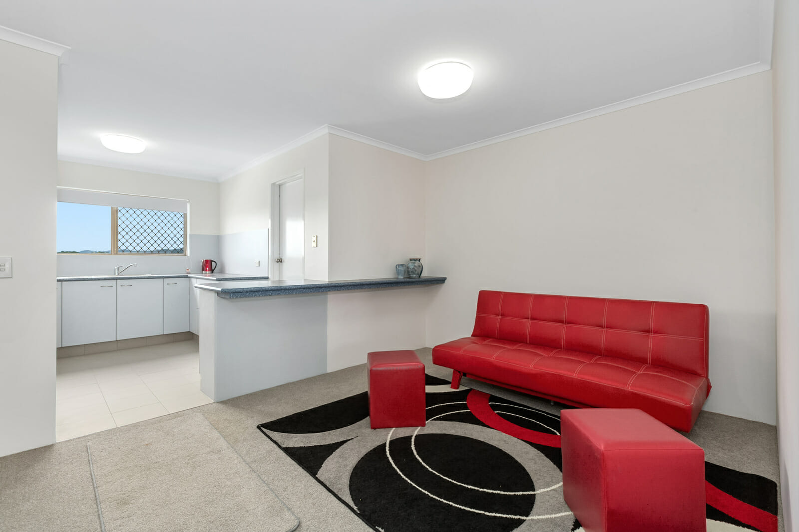 Sitting room with a red couch, adjoining kitchen area