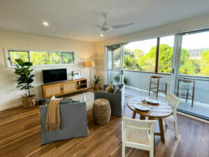 Open plan living area with two armchairs, dining table for two and galley kitchen.